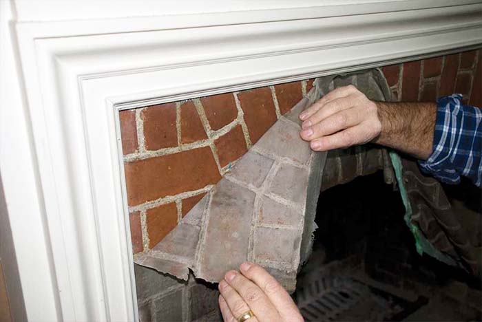 man's hands pulling in a brick paper peeling down from corner of a fireplace