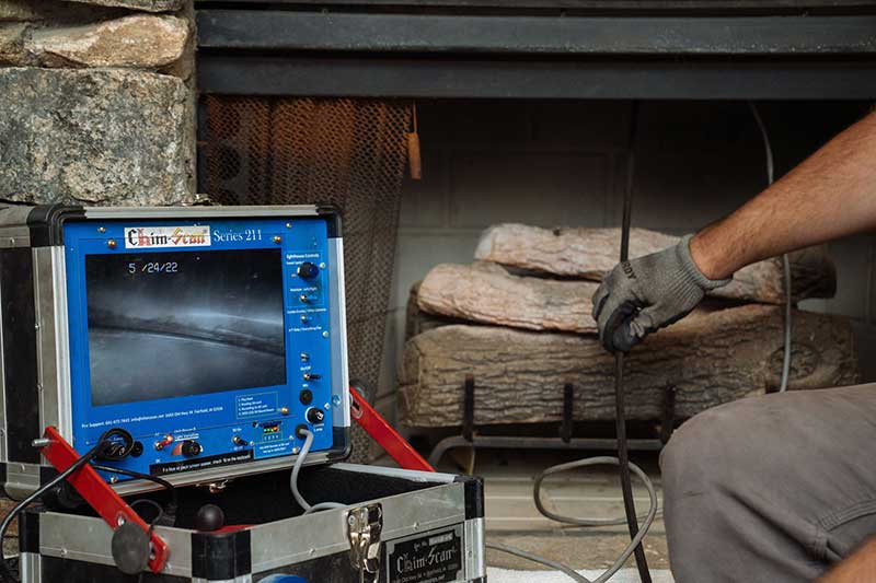 man's hand with glove sitting next to fireplace. A chimney scan video insepection screen set up to the left