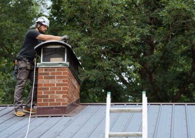 Technician on a roof standing next to a brick chimney inspecting the cap