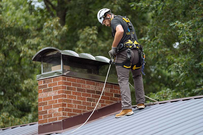 Chimney tech with helmet and harness on roof checking his rope while working on chimney