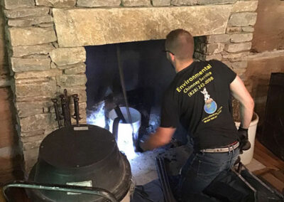 Man kneeling by fireplace using a chimney sweeping tool to sweep the inside